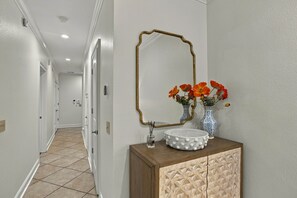 Een hal met een wastafelmeubel, een spiegel, een vaas met bloemen en een decoratieve kast.
