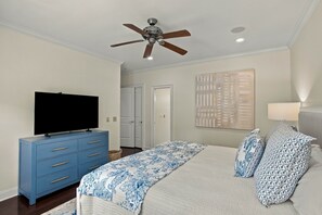 Een slaapkamer met een bed, een televisie op een dressoir, een plafondventilator en een deur.
