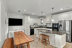 A modern kitchen with white cabinetry, stainless steel appliances, a wooden dining table, and a built-in island with bar stools. - War Eagle Manor:Your Auburn Getaway (Auburn)