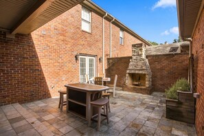 A brick patio with a stone fireplace, a wooden table, and chairs. - War Eagle Manor:Your Auburn Getaway (Auburn)