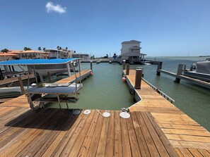 Eine Holzsteg mit überdachter Sitzgelegenheit, einem kleinen Gebäude und freiem Blick auf das Wasser.