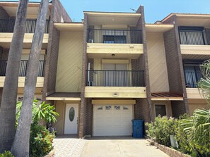 Un edificio residencial de varios pisos con balcones, garaje y entrada protegida por un portón.