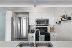 A modern kitchen with stainless steel appliances, white cabinetry, and a built-in microwave. - Walk to the Beach | Pool, Pickleball & Tennis SPI Permit #2025-0205 (South Padre Island)