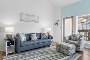 A modern living room with a grey sofa, matching ottoman, and a side table with a lamp. - Walk to the Beach | Pool, Pickleball & Tennis SPI Permit #2025-0205 (South Padre Island)