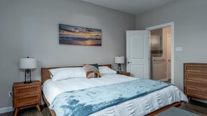 A bedroom with a bed, bedside lamps, a door to a bathroom, and a painting on the wall.