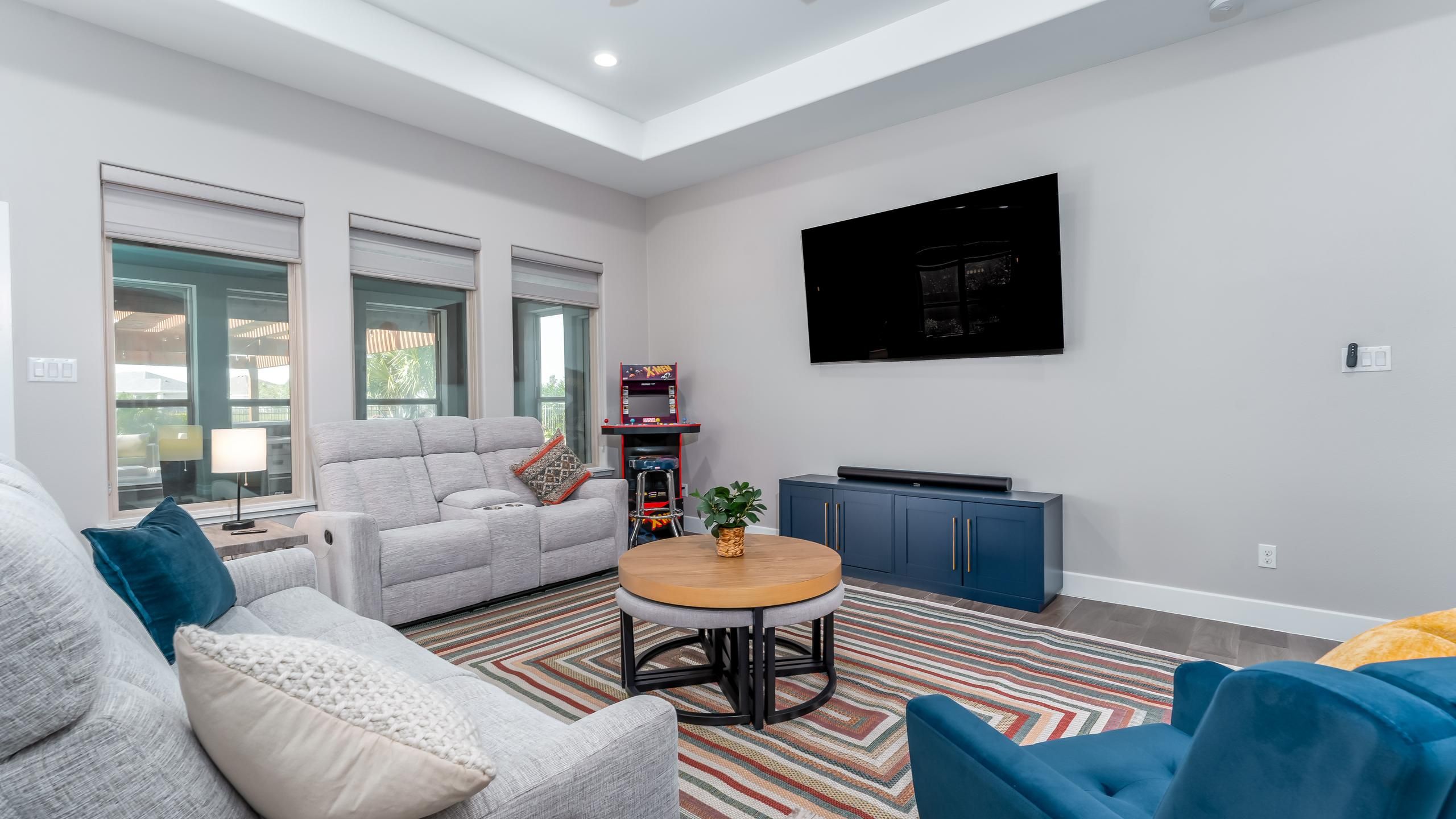 Ein modernes Wohnzimmer mit einem grauen Sofa, blauen Sesseln, einem Couchtisch und einem an der Wand befestigten Flachbildfernseher.