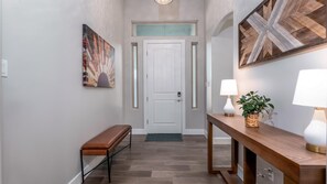 A hallway with a bench, a door, and a table with lamps and a plant.