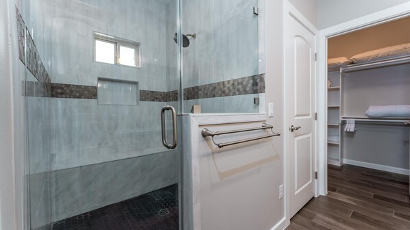 A bathroom with a glass shower enclosure, a towel rack, and a white door leading to a closet with shelves.