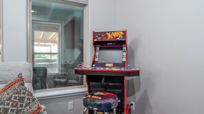 A gaming arcade with a X-Men theme, including a joystick and buttons, in a room with a window and a couch.