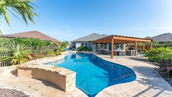 A swimming pool with a curved design, surrounded by a patio area with outdoor furniture and a pergola.