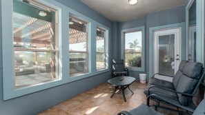 A sunlit room with large windows, a tiled floor, and a seating area with a table and chairs.