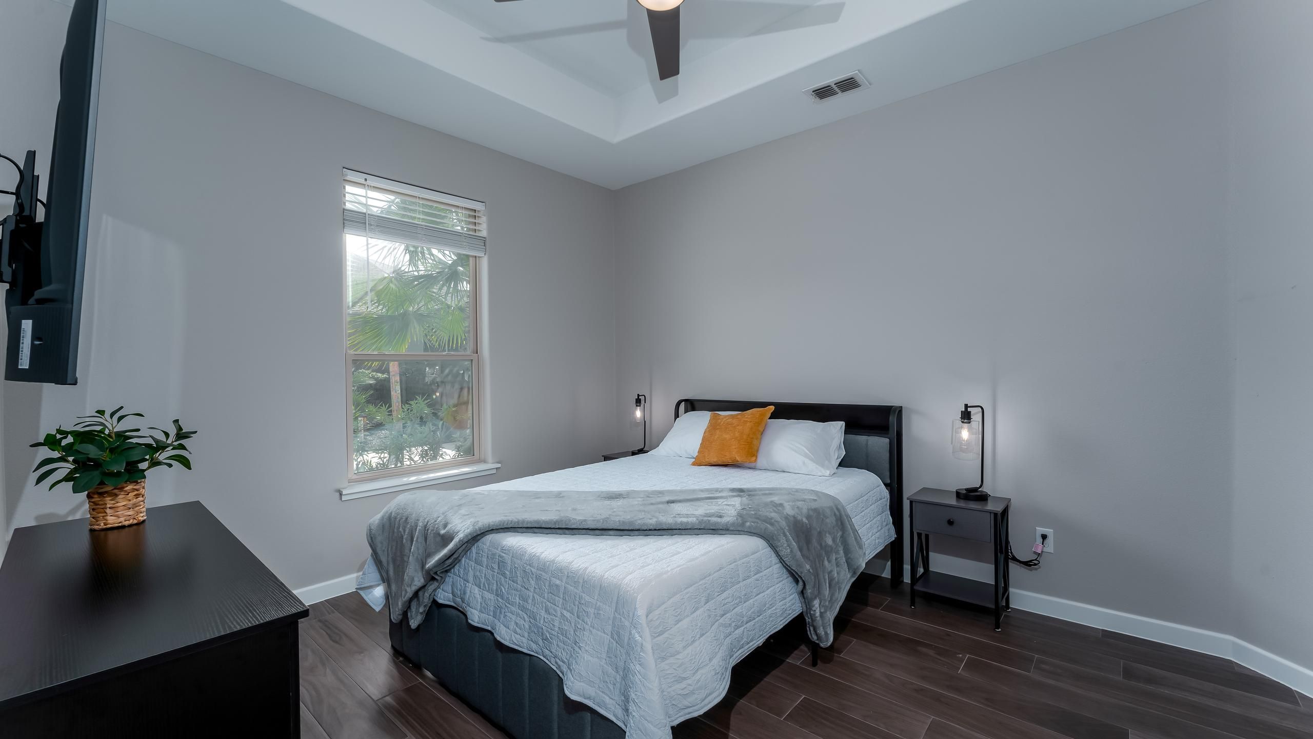 Une chambre à coucher avec un lit, des tables de chevet, une commode, une fenêtre et une plante en pot.