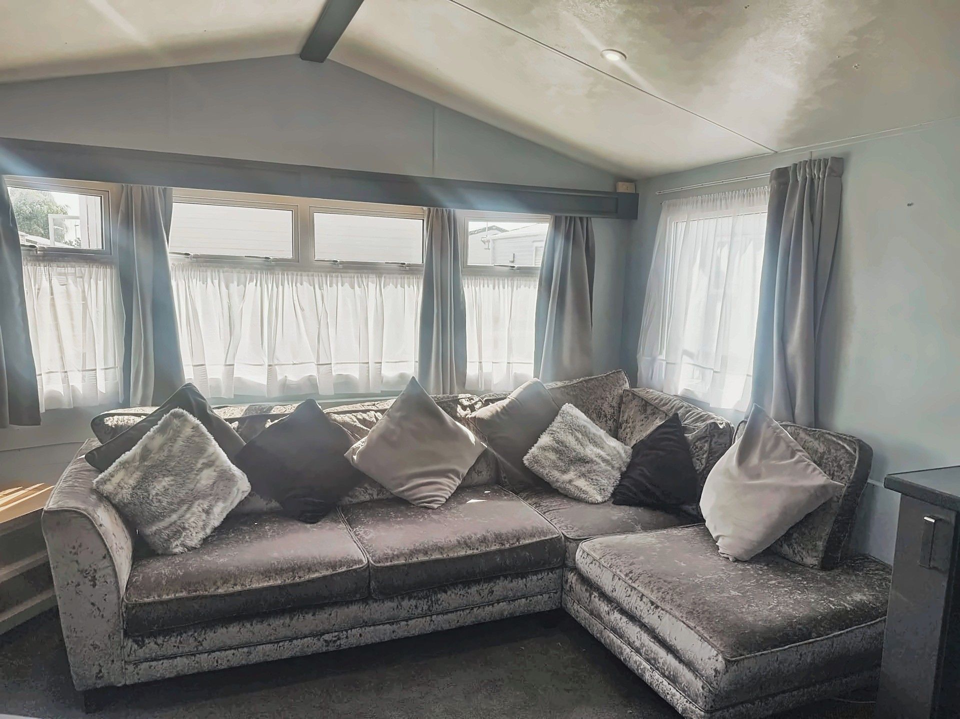 A corner sofa with multiple cushions, a window with curtains, and a ceiling with a light fixture.