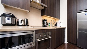 A modern kitchen with a built-in oven, a microwave, a coffee maker, and a refrigerator. - RivetStays | The Atmos Gorgeous Suite – 1 Bedroom Condo (Toronto)