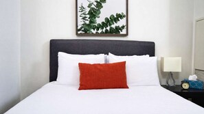 A neatly made bed with white and red pillows, a dark headboard, and a framed plant on the wall. - RivetStays | The Atmos Gorgeous Suite – 1 Bedroom Condo (Toronto)