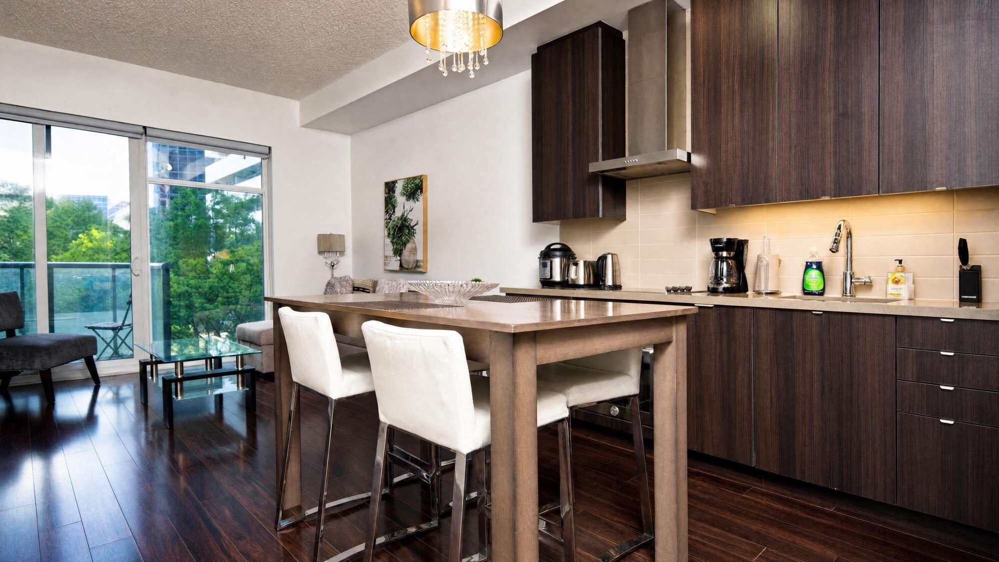 A modern kitchen with a central island, dark wood cabinets, and a large window overlooking greenery.