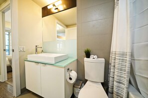 A modern bathroom with a glass-top sink, a toilet, and a shower curtain. - The Atmos by RivetStays – Spacious 2BR Downtown Condo (Toronto)