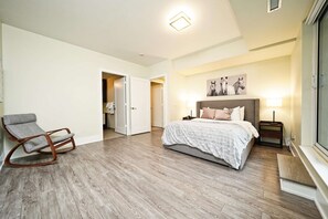 A bedroom with a bed, a chair, a nightstand, and a painting on the wall. - The Atmos by RivetStays – Spacious 2BR Downtown Condo (Toronto)