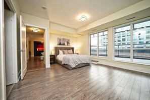 A bedroom with a large window, a bed, and a hallway leading to another room. - The Atmos by RivetStays – Spacious 2BR Downtown Condo (Toronto)