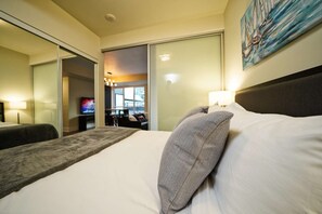 A hotel room with a bed, a TV, a painting, and a view of the outside. - The Atmos by RivetStays – Spacious 2BR Downtown Condo (Toronto)