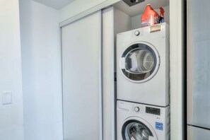 Un appareil combiné lave-linge et sèche-linge, avec un panneau de commande et un flacon de lessive placés sur le dessus.