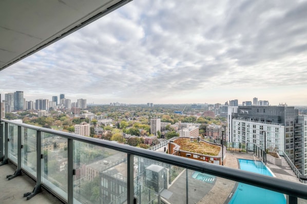 Un immeuble de grande hauteur doté d’un balcon en verre qui offre une vue panoramique sur la ville, avec ses différents bâtiments et un parc.