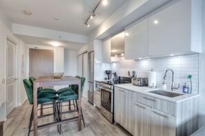 A modern kitchen with a central island, stainless steel appliances, and a dining area with green velvet chairs. - RivetStays | The Jarvis Premier Suite – 2 Bedroom Suite (Toronto)