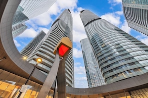 A modern urban skyline with high-rise buildings, a curved glass structure, and a street lamp. - RivetStays | The York Standard Suite – 1 Bedroom Condo (Toronto)