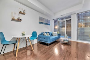 Una sala de estar moderna con un sofá azul, una mesa de centro redonda y un comedor con una mesa blanca y sillas azules.