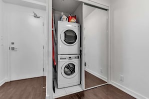 Un cuarto de lavandería con dos lavadoras apiladas y una puerta que da a otra habitación.