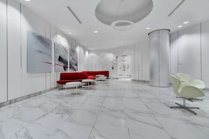 A modern lobby with a red sofa, white chairs, and a marble floor. - RivetStays | The York Standard Suite – 1 Bedroom Condo (Toronto)
