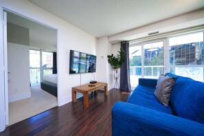 A modern living room with a blue sofa, a wooden coffee table, and a flat-screen TV mounted on the wall. - RivetStays | The Atmos Presidential Suite – 2 Bedroom Condo (Toronto)
