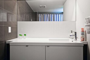 A modern bathroom with a white sink, chrome faucet, and a mirror above it. There are two bottles on the sink and a towel hanging on the wall. - RivetStays | The Atmos Presidential Suite – 2 Bedroom Condo (Toronto)