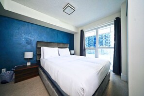 Una habitación de hotel moderna con una cama grande, una mesita de noche, una lámpara y vistas a la ciudad desde la ventana.