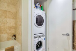 A laundry room with two front-loading washing machines and a door to a bathroom. - RivetStays | The York Romantic Suite – 1 Bedroom Condo (Toronto)