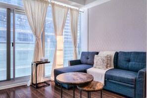 A modern living room with a blue sofa, a round wooden table, and a floor lamp. - RivetStays | The York Romantic Suite – 1 Bedroom Condo (Toronto)