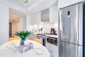 A modern kitchen with stainless steel appliances, a marble countertop, and a potted plant. - RivetStays | The Jarvis Royal Suite – 2 Bedroom Suite (Toronto)