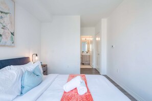 Hotellihuone, jossa on sänky, yöpöytä, taulu ja kylpyhuone, joka näkyy avoimesta ovesta.