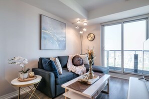 Un salon moderne avec un canapé gris foncé, une table basse ronde et une grande fenêtre donnant sur la ville.