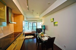 A modern kitchen with a built-in stove, wooden cabinets, and a dining area with a table set for two. - RivetStays | The York Honeymoon Suite – Studio Condo (Toronto)