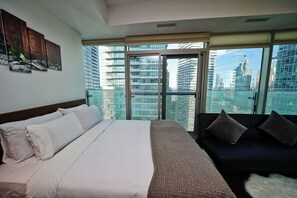 A modern hotel room with a large bed, a sofa, and a balcony with a city view. - RivetStays | The York Honeymoon Suite – Studio Condo (Toronto)