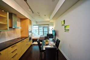 A modern kitchen with built-in appliances, a dining area with a table set for two, and a large window offering a city view. - RivetStays | The York Honeymoon Suite – Studio Condo (Toronto)