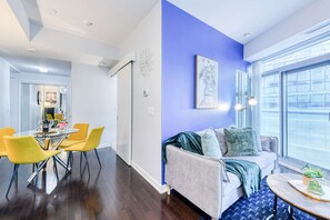 Una sala de estar moderna con una pared azul destacada, un sofá con cojines, una mesa de centro y un comedor con sillas amarillas.