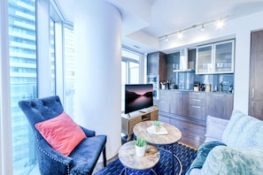 Una sala de estar moderna con un ventanal grande, un televisor de pantalla plana, un sillón azul, una mesa de centro redonda y un sofá.