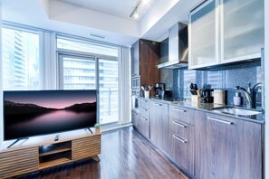 A modern kitchen with a large window, built-in oven, microwave, and a flat-screen TV on a wooden stand. - RivetStays | The York Premier Suite – 1 Bedroom Condo (Toronto)