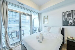 A hotel room with a large bed, a view of the outside balcony, and a framed picture on the wall. - RivetStays | The York Presidential Suite – 2BR/2BA Condo (Toronto)