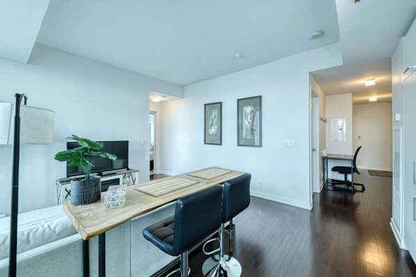 A modern kitchen with a wooden countertop, two bar stools, a potted plant, and a television. - RivetStays | The York Presidential Suite – 2BR/2BA Condo (Toronto)