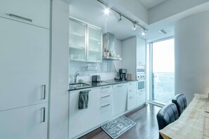 A modern kitchen with white cabinets, a black countertop, and a coffee machine. - RivetStays | The York Presidential Suite – 2BR/2BA Condo (Toronto)