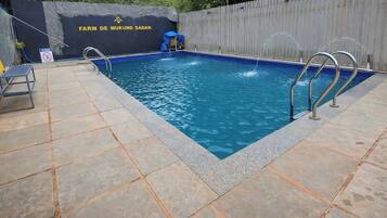 Ein rechteckiger Swimmingpool mit blauer Innenseite, umgeben von einer gefliesten Terrasse.