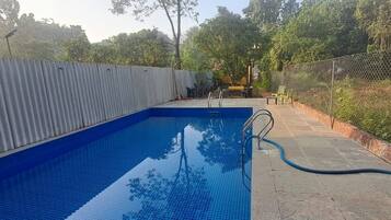 Une piscine rectangulaire aux parois recouvertes de carreaux bleus, entourée d’une terrasse en béton et d’une clôture en métal.